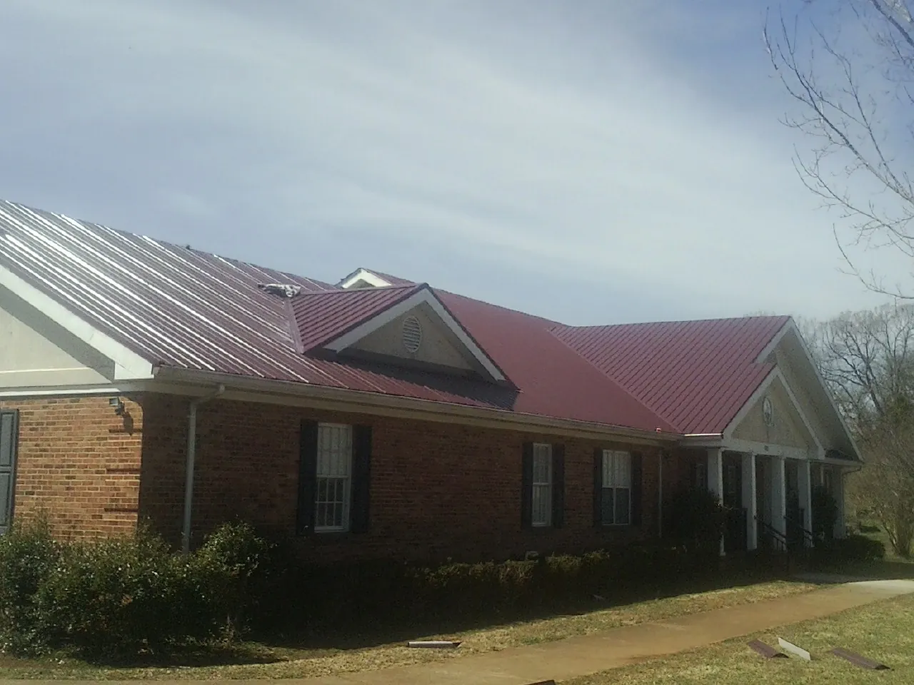 Red metal roof with gabled entries on a long brick building, from a Hail Damage Roof Repair job in Olustee
