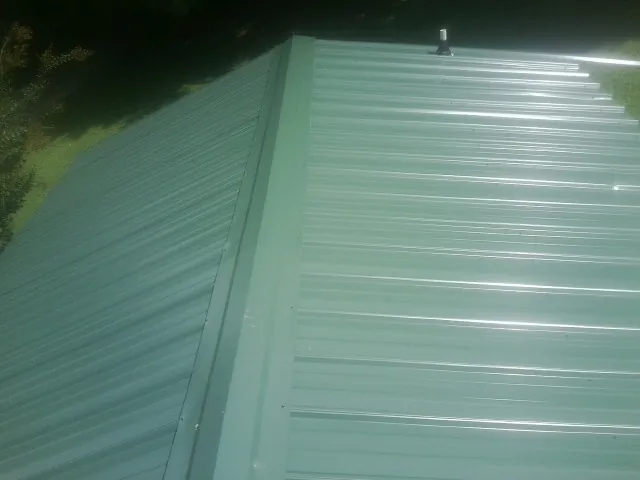 New green metal panels meeting at the ridge of a roof — Flat Roof Repair work by our crew in Olustee