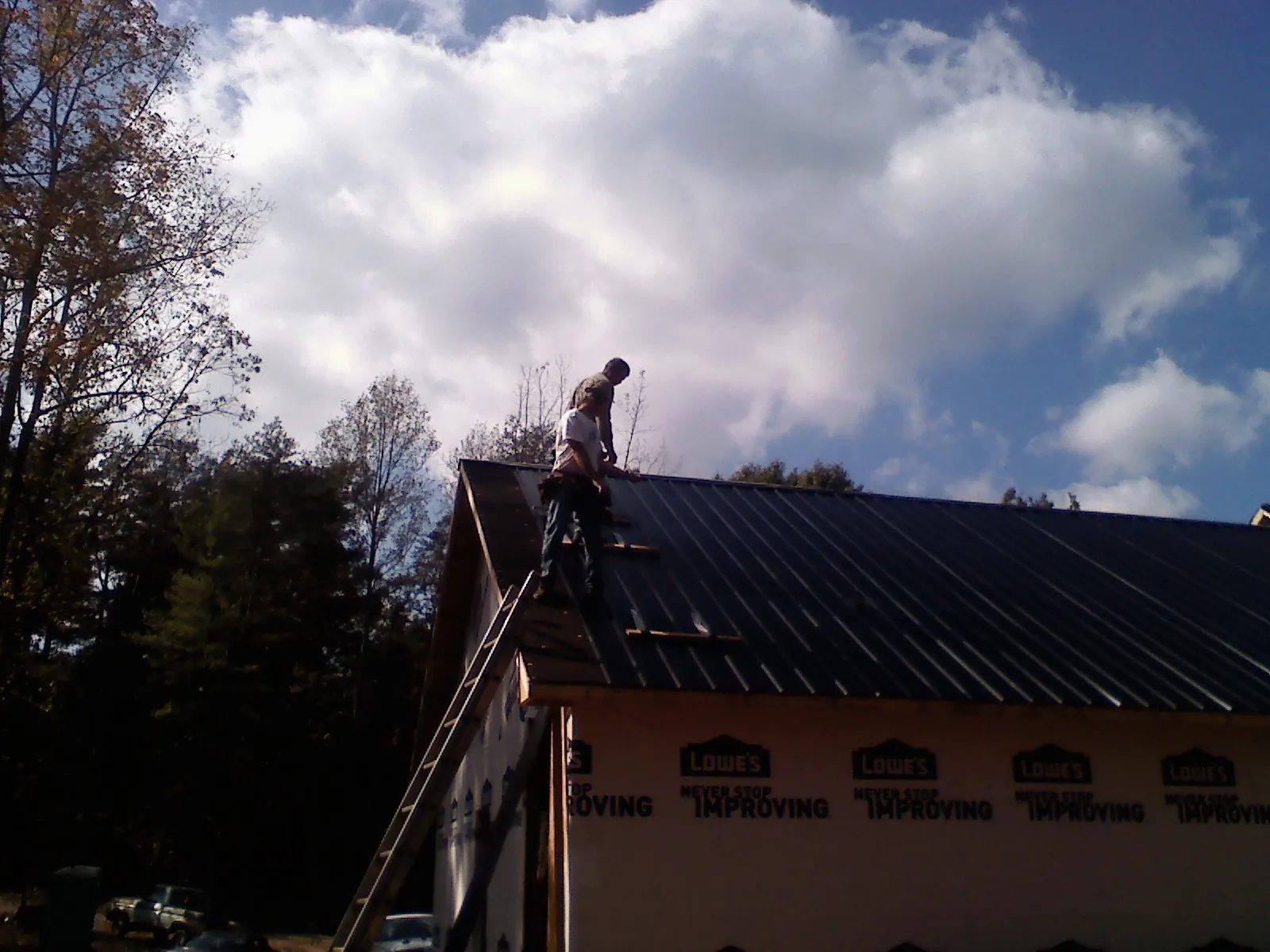Roofer fastening dark metal panels high against a cloudy sky, from a Roof Inspection job in Olustee