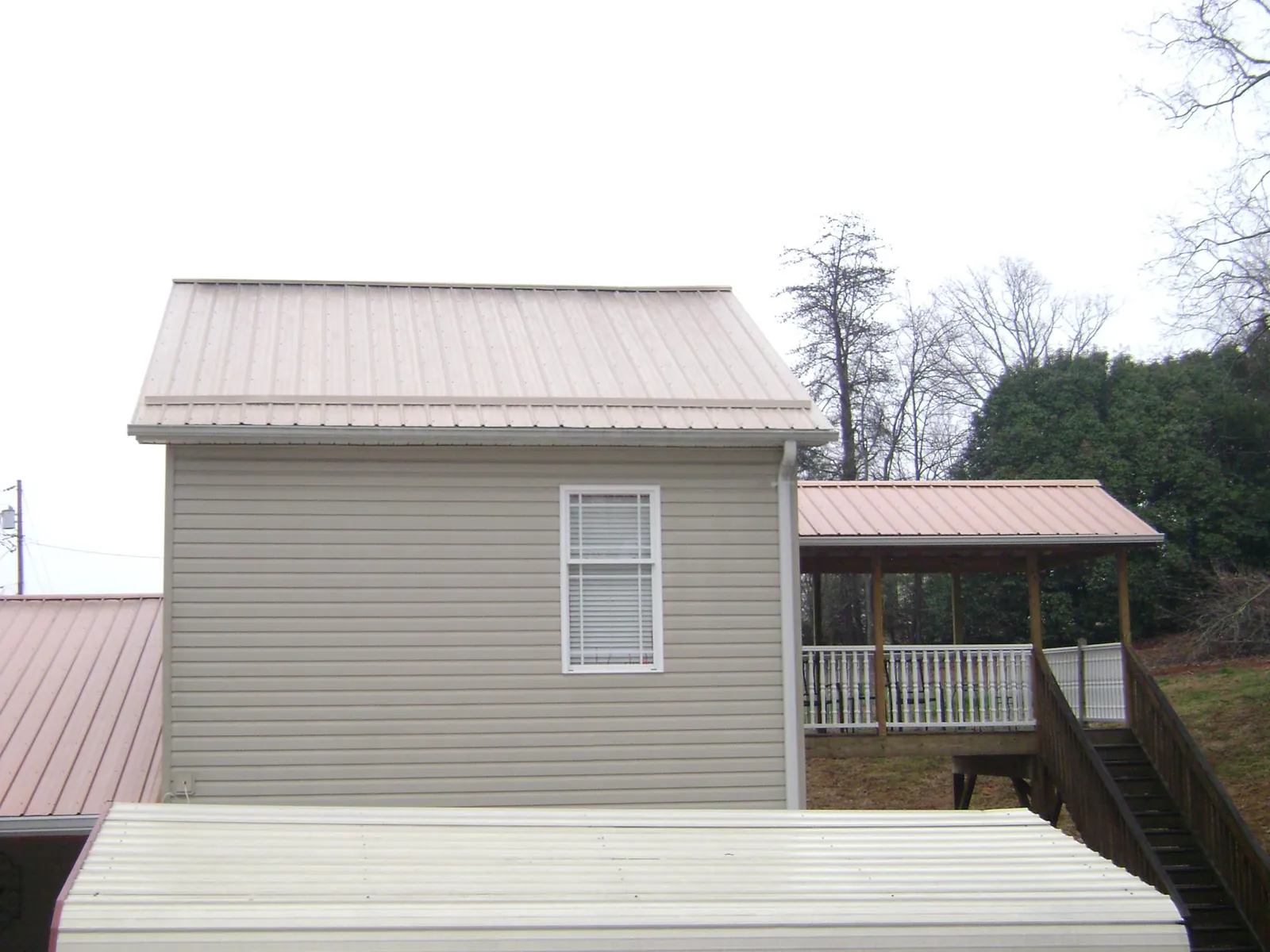Tan metal roofs on a two story addition and attached porch, from a Roof Replacement job in Olustee